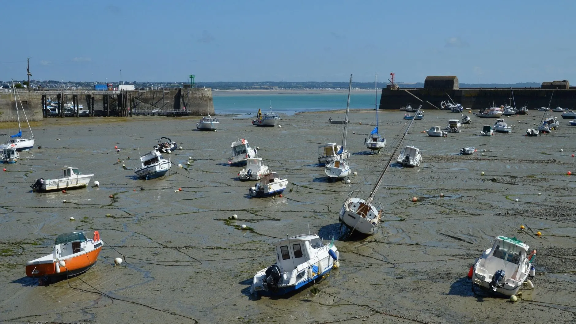 Small boats lying on the mud of a walled harbour at low tide, mooring lines slack