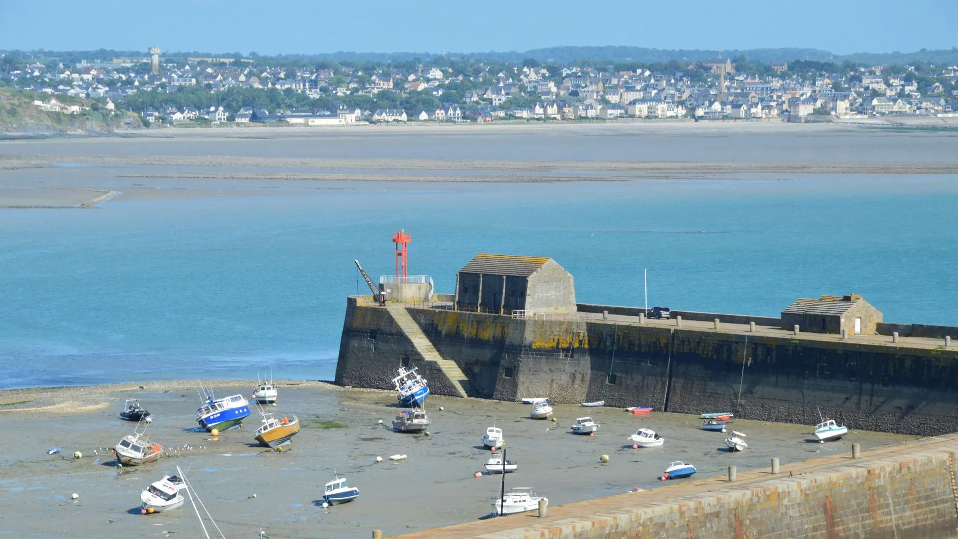 Boats sitting on the harbour floor inside the stone pier at low water, with the town across the bay