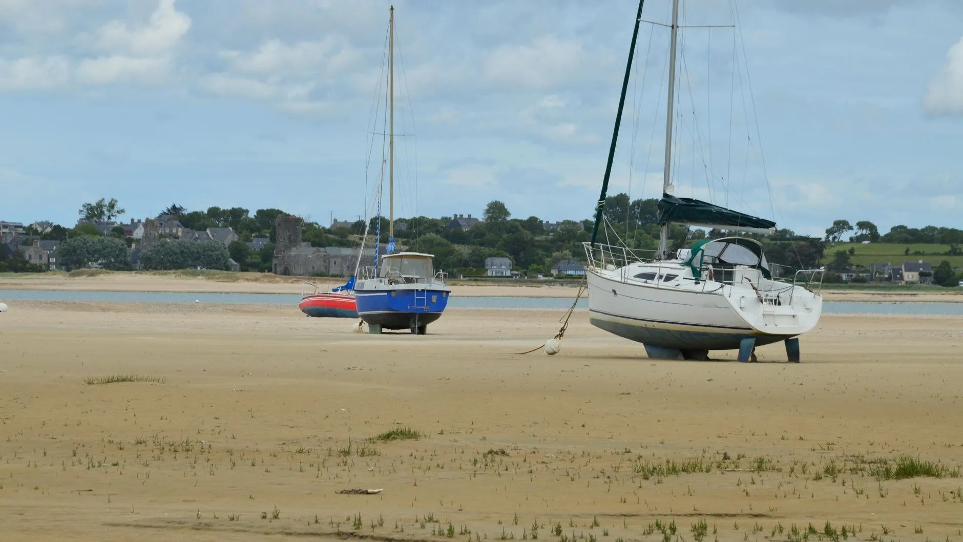 Two yachts and a small motor boat sitting upright on a wide sand flat at low tide