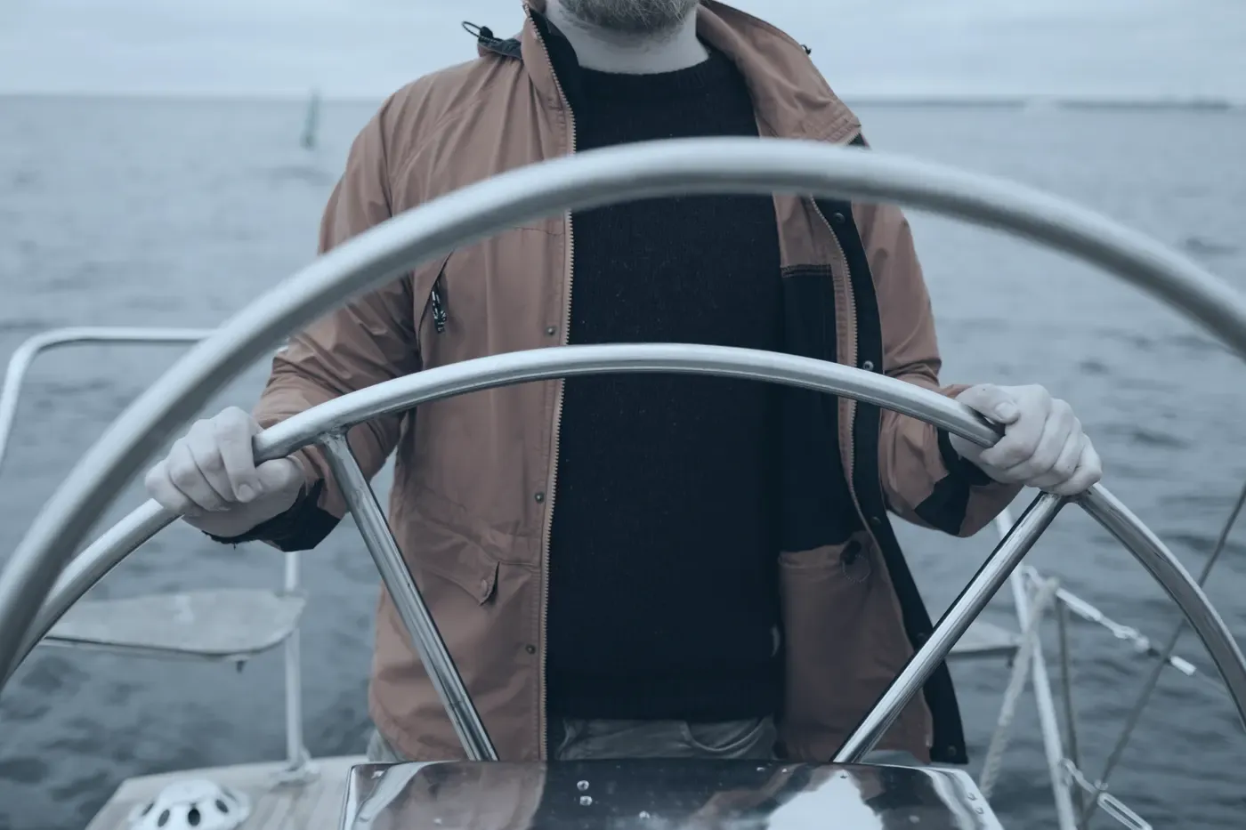 A crew member at the wheel of a small boat under way.